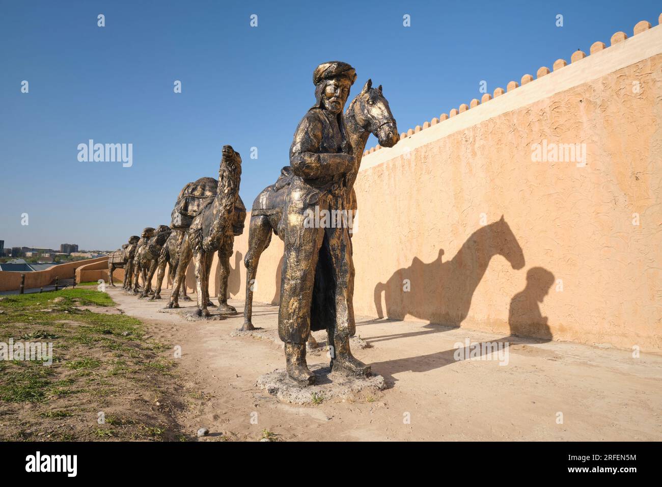 A large bronze sculpture depicting a typical Silk Road caravan scene with camels and horses carrying goods across the desert. At the old fortress, cit Stock Photo