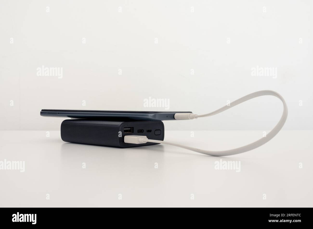 Mobile phone charging from black power bank on the table. White background. Stock Photo