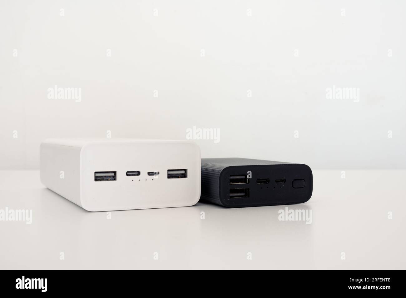 White power bank and black mobile charger on the table. White background. Stock Photo