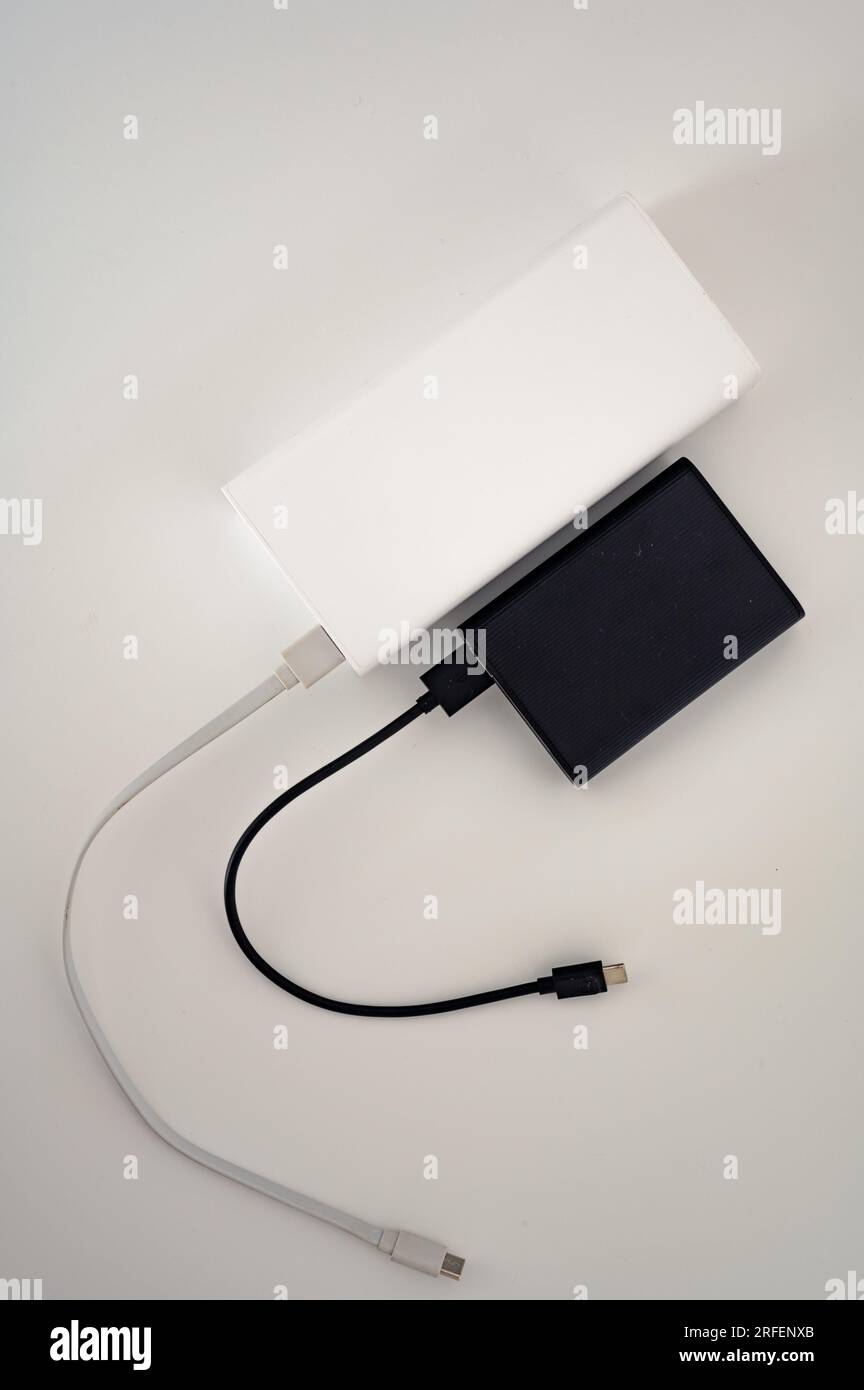 Black power bank parallel to white mobile charger with white and black cord cable connected. White background. Stock Photo