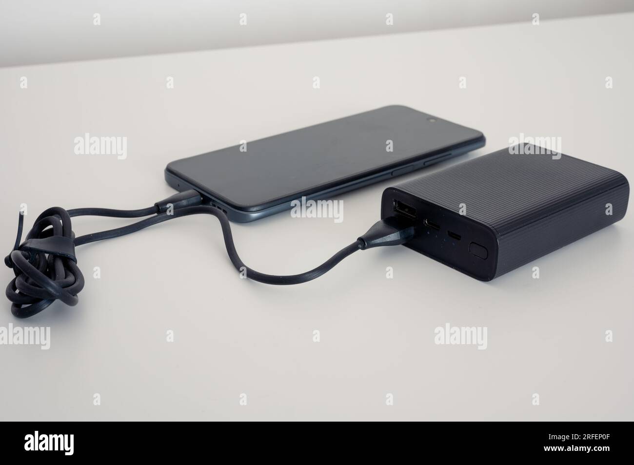 Black power bank charges mobile. Black cable. Both on the white