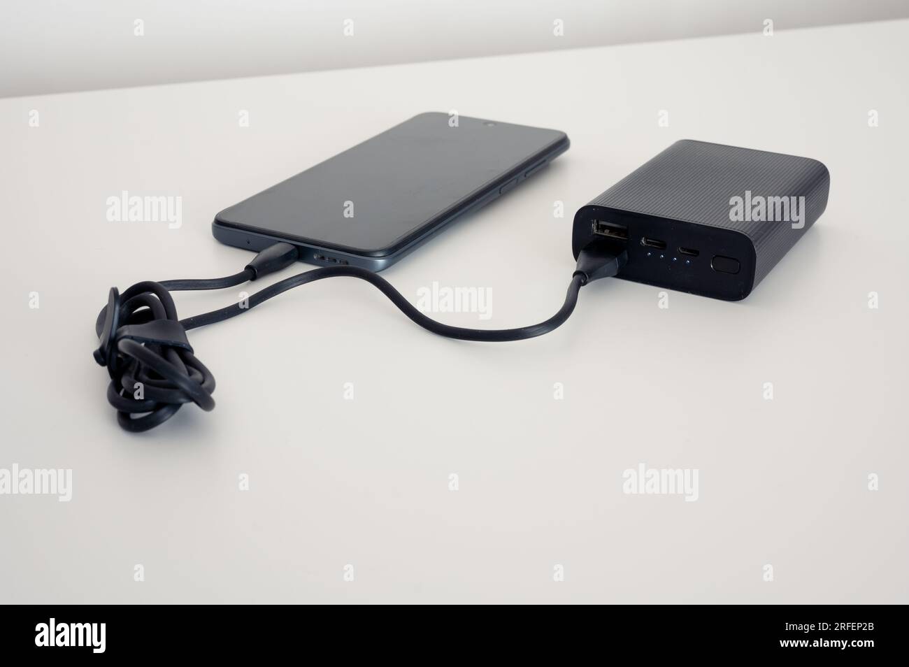 Black power bank charges mobile phone. Black cable. Both on the white
