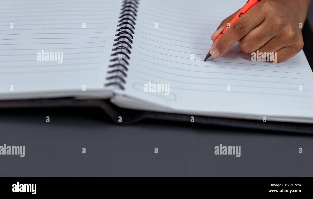 A closeup photo of a kid, writing in a notebook. He is lefthanded and