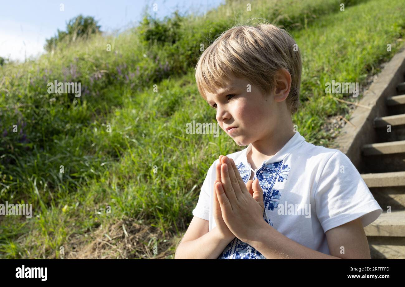 7-year-old boy in a vishyvanka, hands folded in prayer, an appeal to God. Dreams of peace for homeland Ukraine. Children are asked to stop the war in Stock Photo