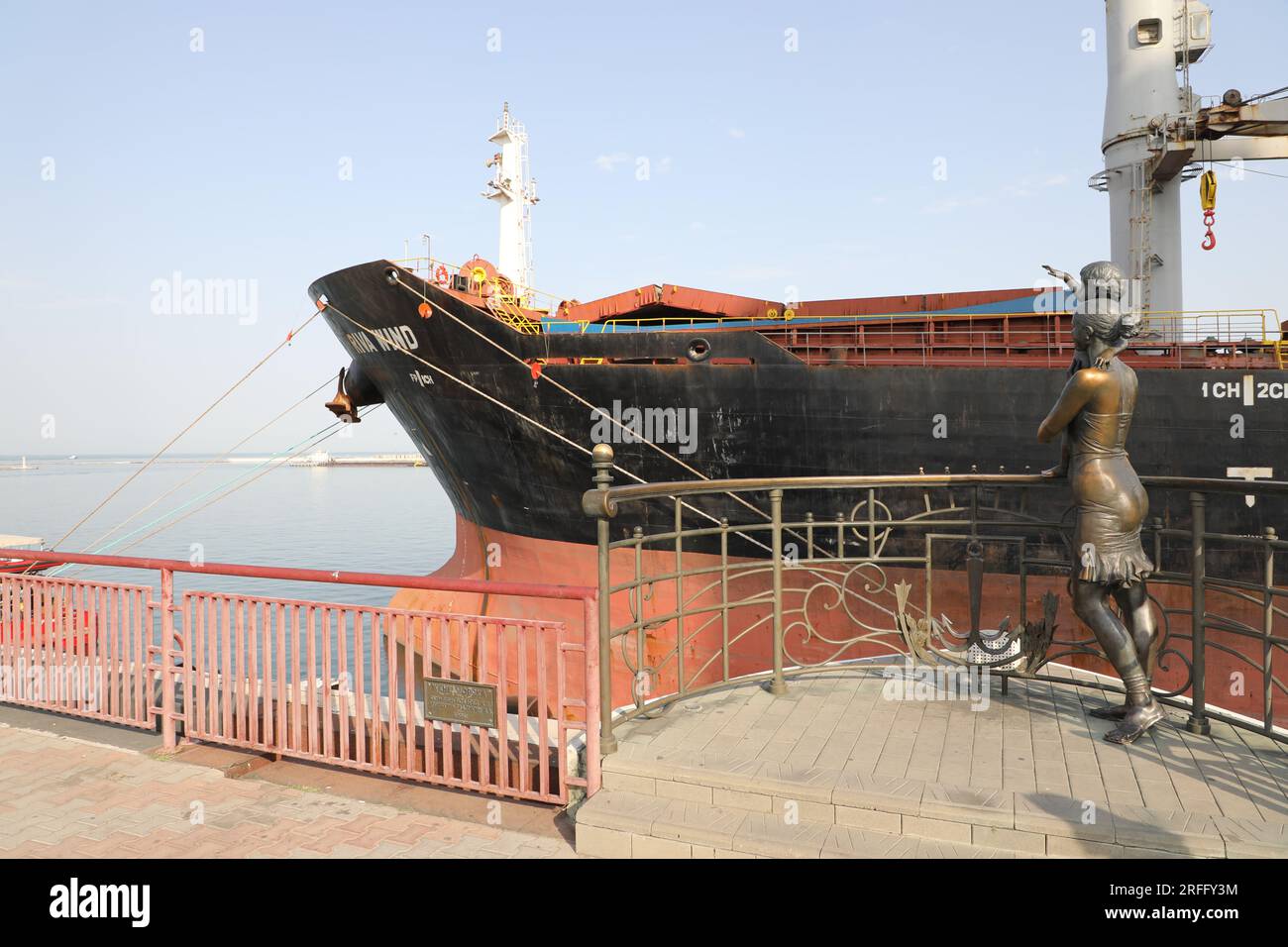 Statue of sailor's wife and child by A.P. Tokarev at the waterfront in the port area of Odesa (Odessa) in Ukraine with a large ship; farewell concept Stock Photo