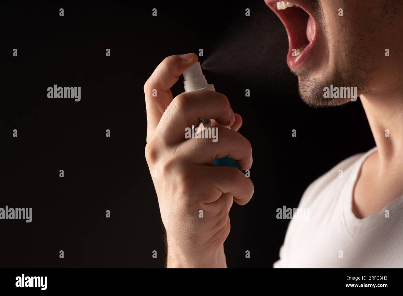 Man with open mouth spray his throat isolated on black background Stock Photo