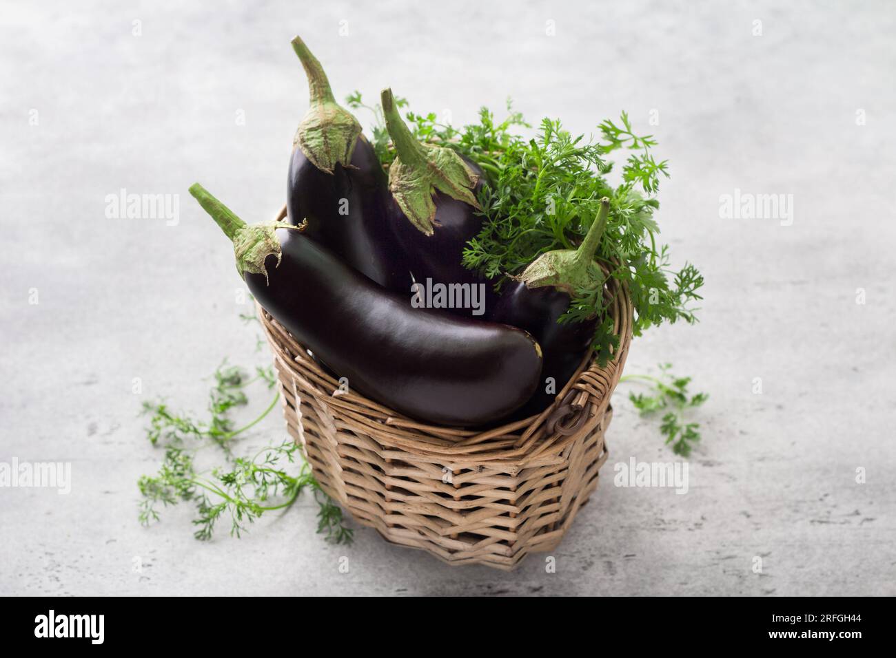 Wicker basket with ripe eggplants and herbs on a gray textured background. Stock Photo