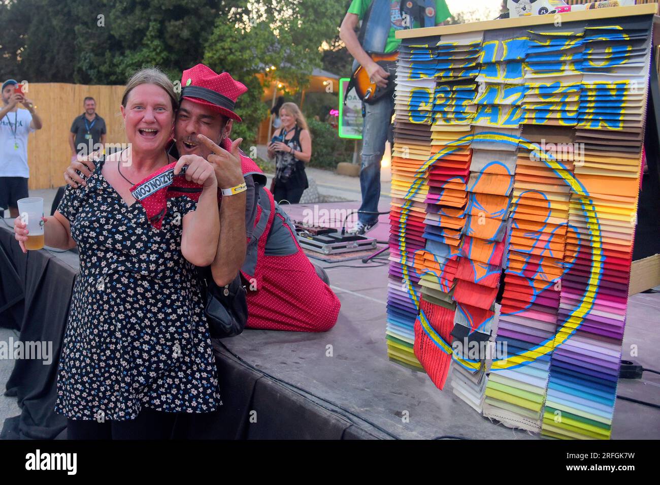 Mano creaZion poses with a woman in the audience during his performance at the Jardins de Terramar Festival in Sitges. The band of musicians Coser y Cantar Music (Sew and Sing  Music) and its leader Manu creaZion accompanied by his sewing machine goes on stage and during the show creates unique pieces to the rhythm of the music. A hat, a bag, a t-shirt. that's what you can take home at the end of the concert, he always gives away his creations to those he sees dance the most A style full of sounds ranging from Hip-Rock to Reggae. Stock Photo