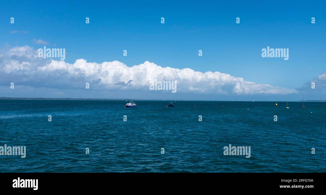 White billowing clouds joined together along the horizon at Yarmouth, Isle of Wight, England, Uk Contrasting with rich blue sea. Stock Photo