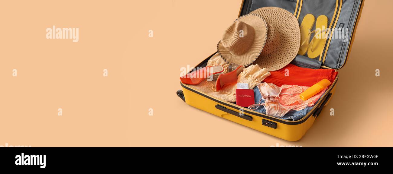 Open suitcase with clothes, passport and ticket on beige background