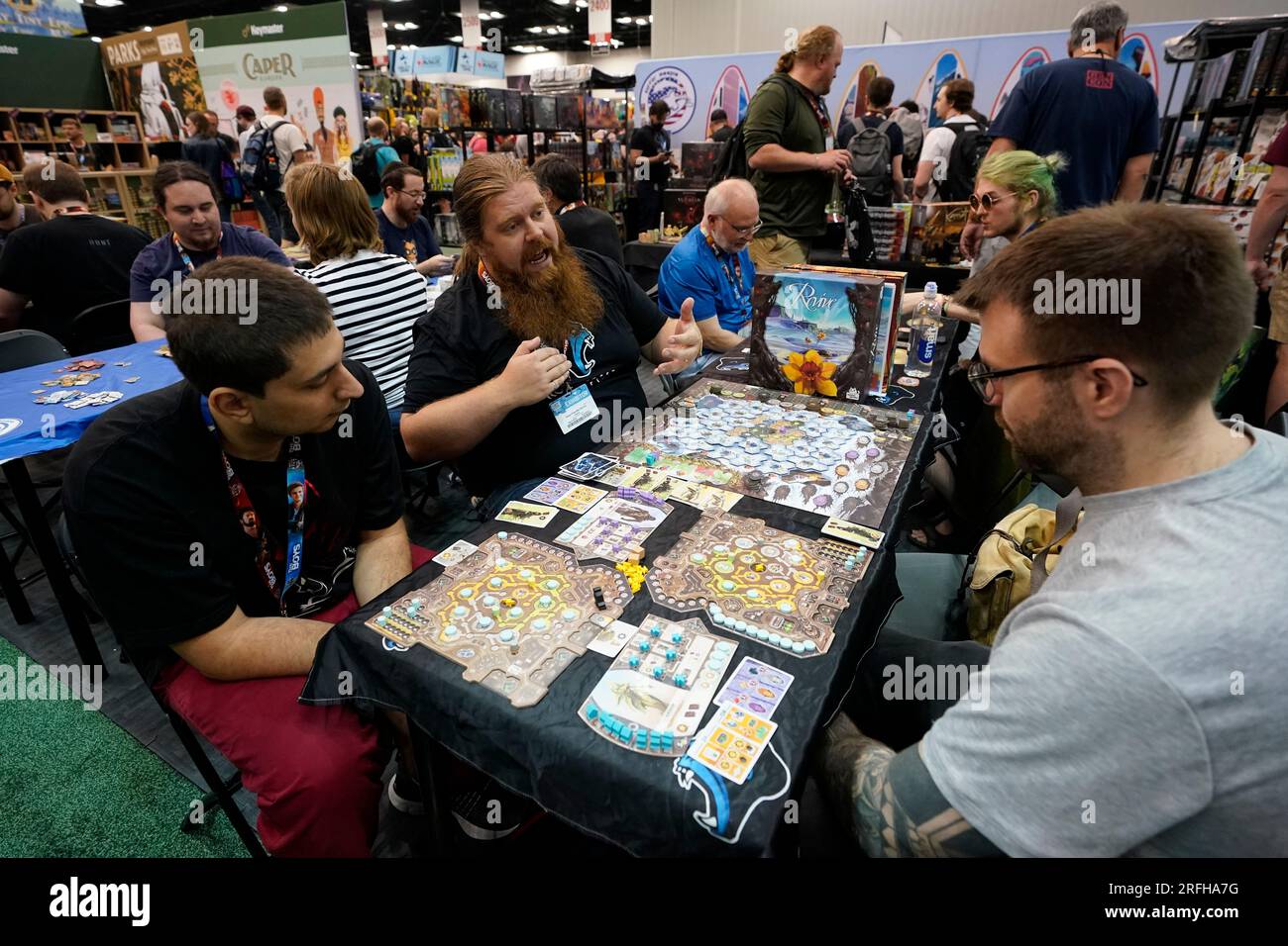 Greg Chandler Burns, center, explains a board game to guest during the Gen Con convention