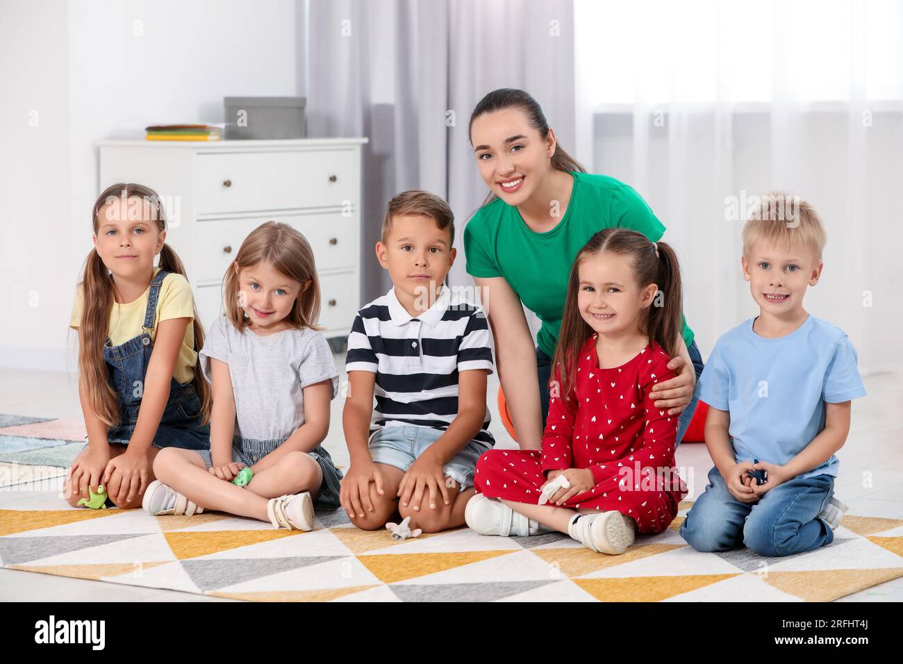 Nursery teacher and group of cute little children on floor in