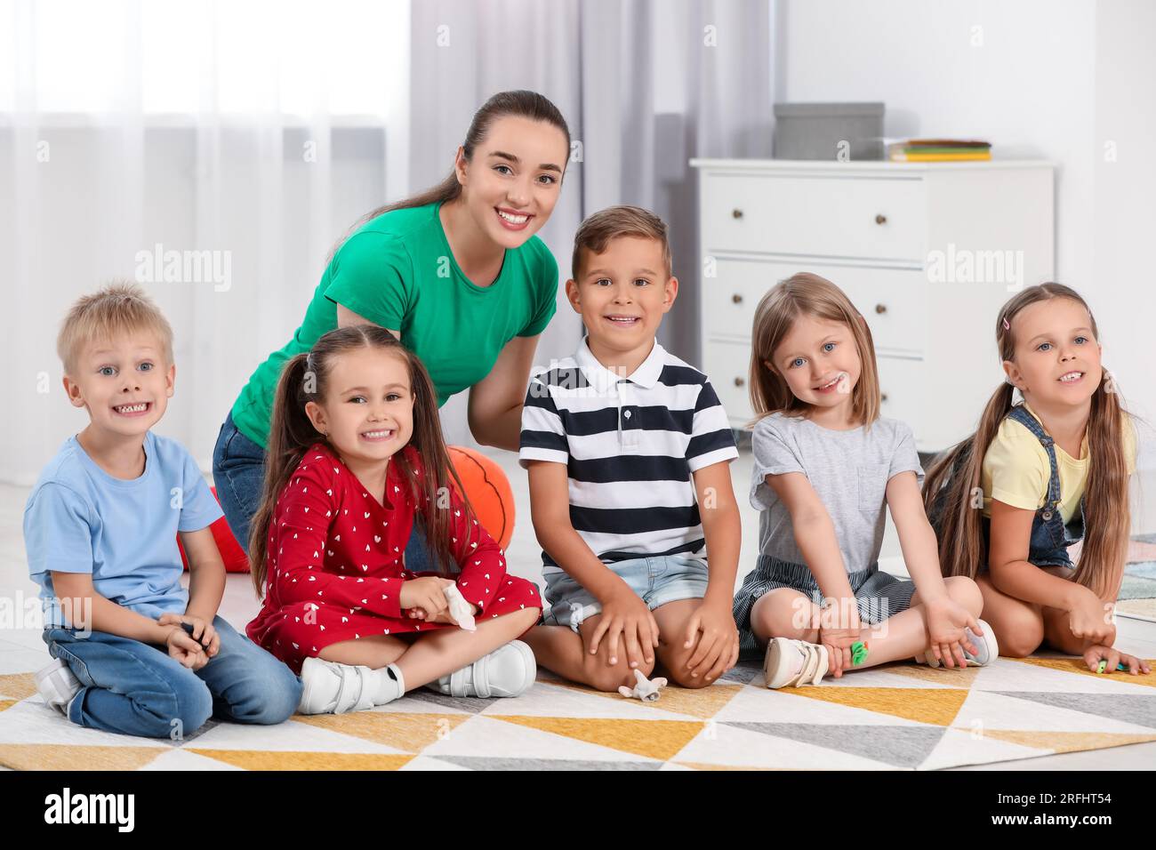 Nursery teacher and group of cute little children on floor in