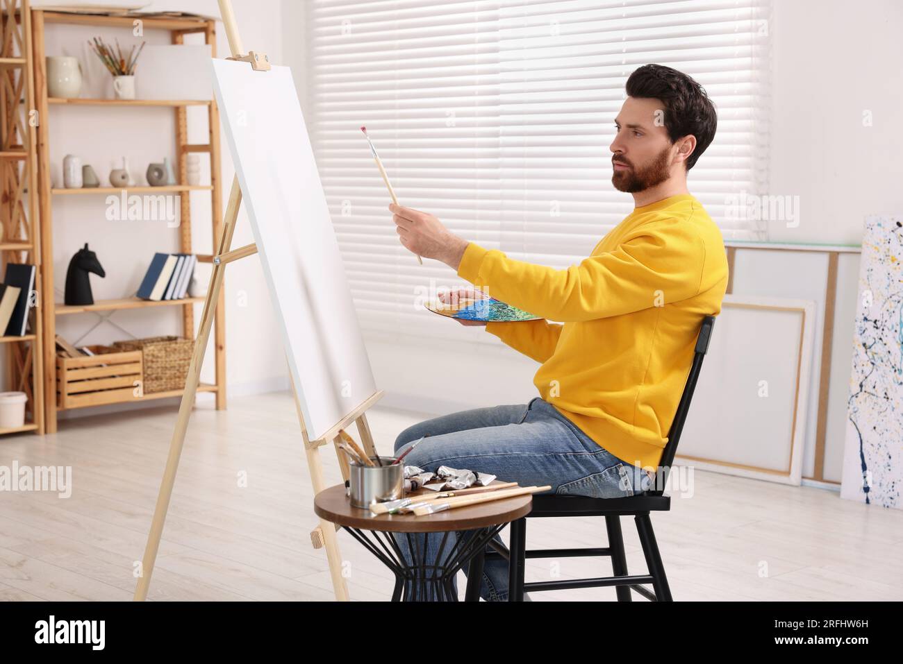 Man painting in studio. Using easel to hold canvas Stock Photo - Alamy
