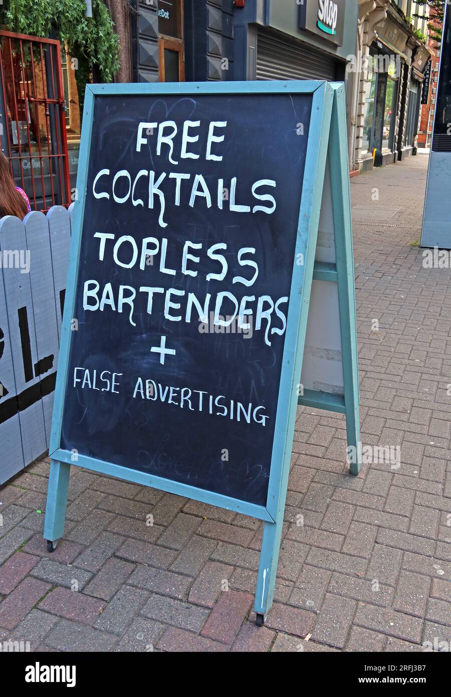 Humorous chalkboard A-frame sign outside a bar advertising “Free cocktails” and “topless bartenders” before revealing “false advertising”, UK. Stock Photo