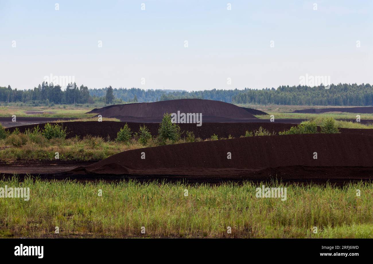 the flooded area where peat is extracted, black peat is stacked in huge piles for loading on transport Stock Photo