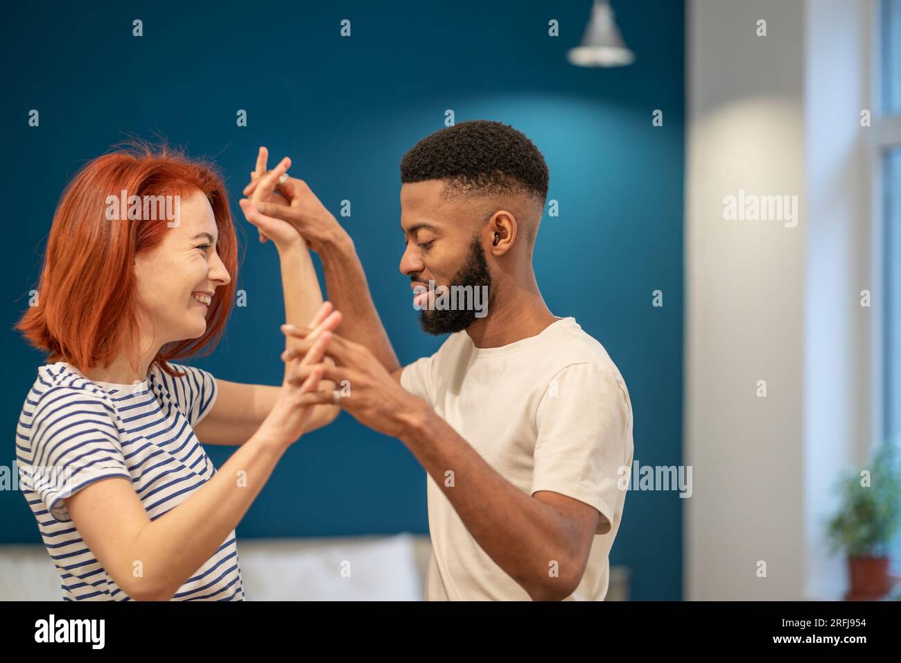 Loving young diverse couple dancing romantic dance in modern bedroom with panoramic windows. Stock Photo