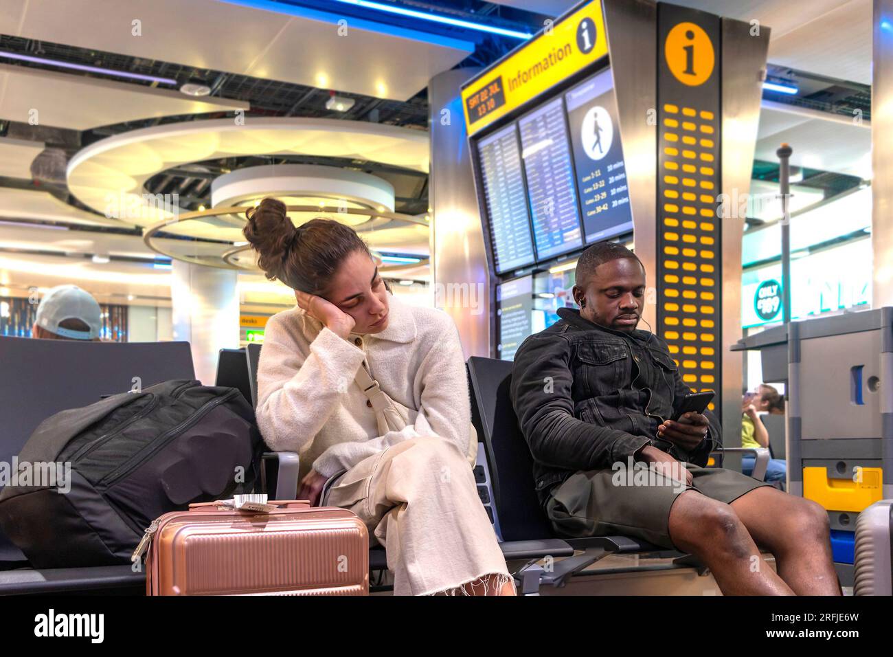 man and woman passenger waiting for flight at departures heathrow airport london uk LHR travel disruption and flight delays concept Stock Photo