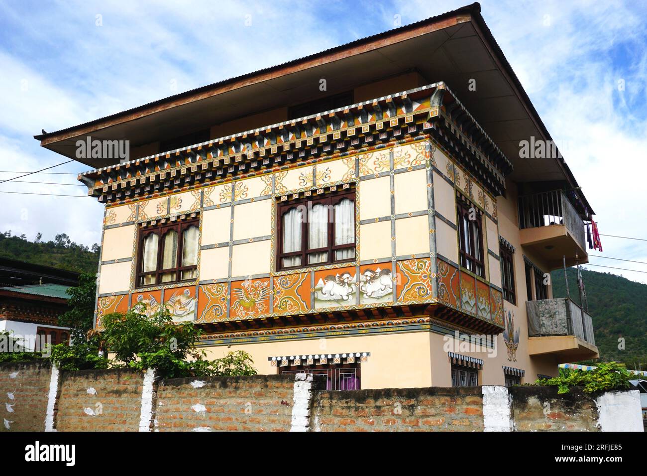 Typical Bhutanese architecture with square overhanging roof, timber framing, painted protruding rafters, triplet windows and decorative painted murals Stock Photo