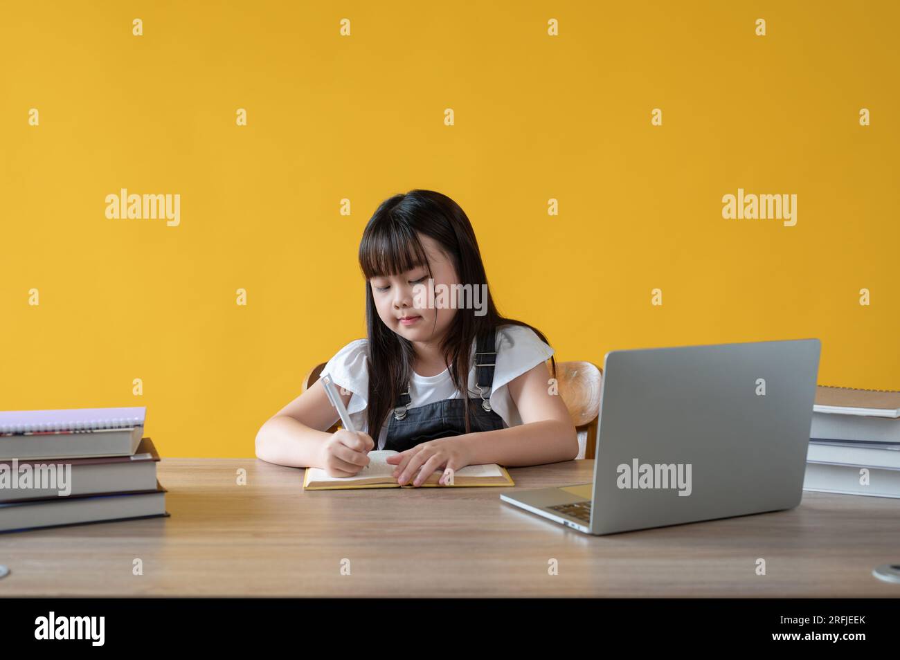 An adorable young Asian girl is doing homework at her study table ...