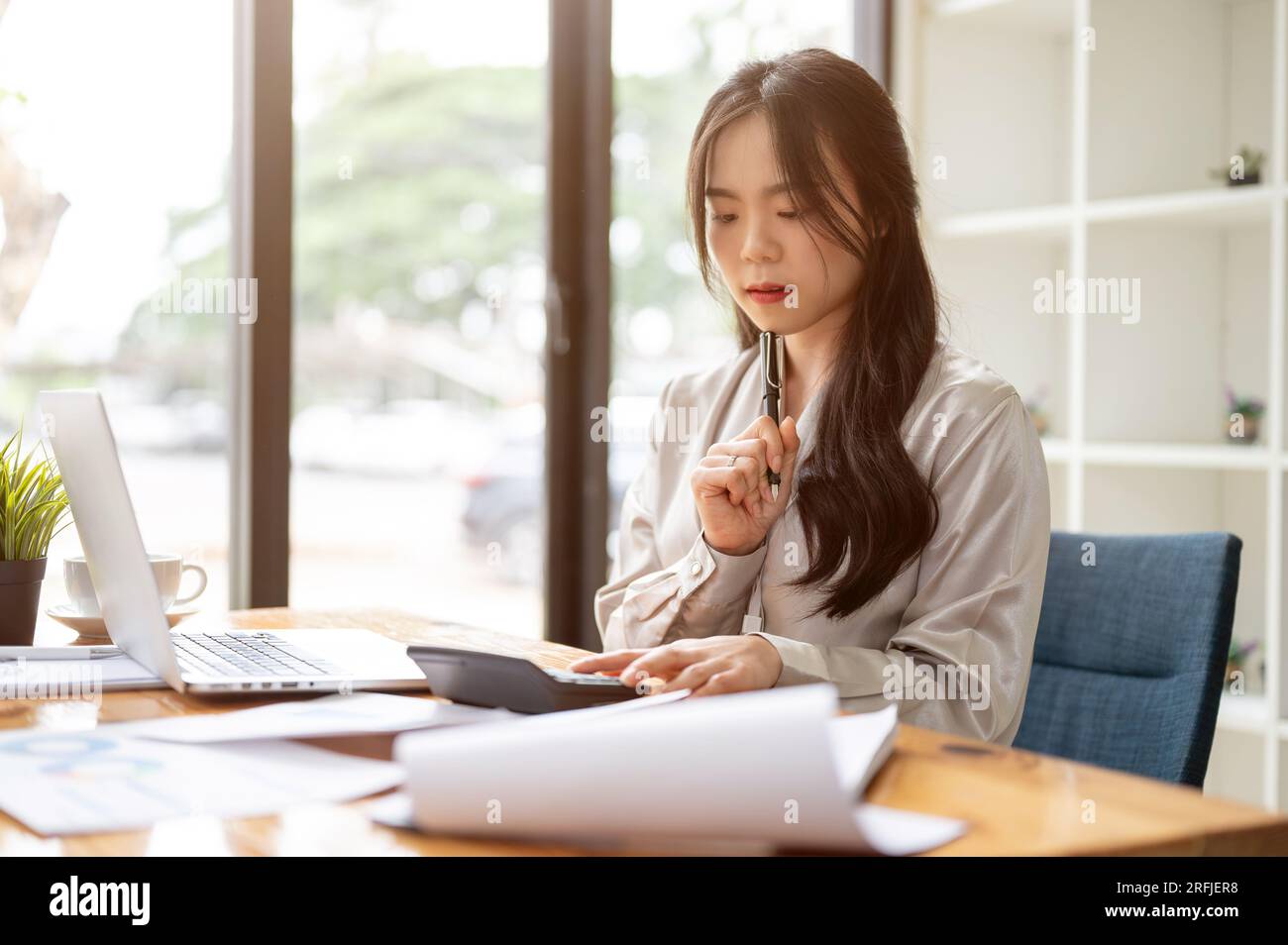 A beautiful and thoughtful Asian businesswoman is focusing on her work ...