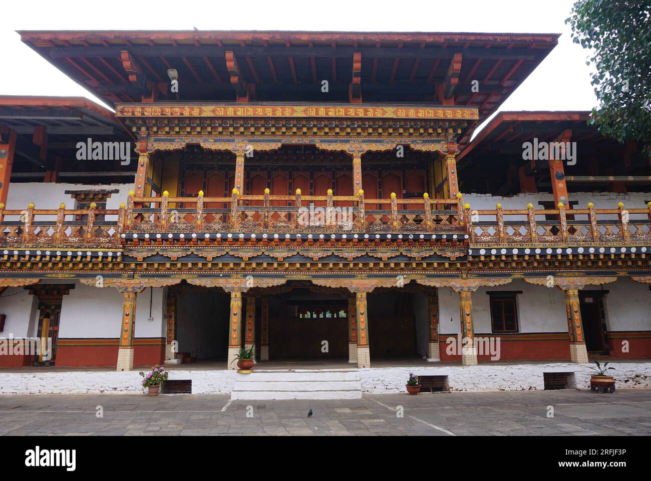 Colorful historic wooden architecture inside Punakha Dzong in Bhutan. A balcony with square overhanging roof sits atop a row of carved painted pillars Stock Photo