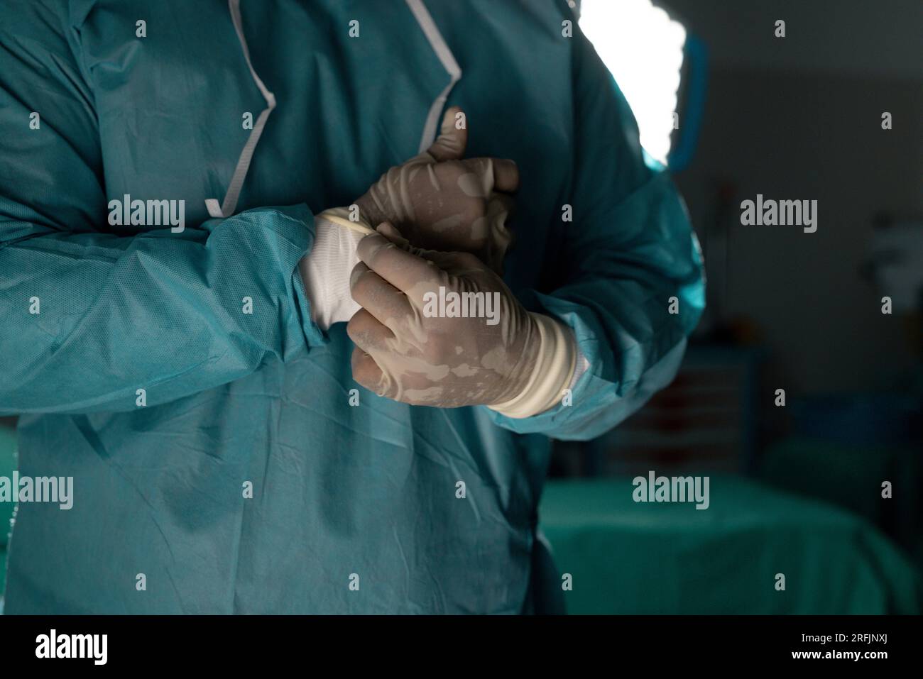 Midsection of biracial male surgeon wearing surgical gown in operating theatre at hospital Stock Photo