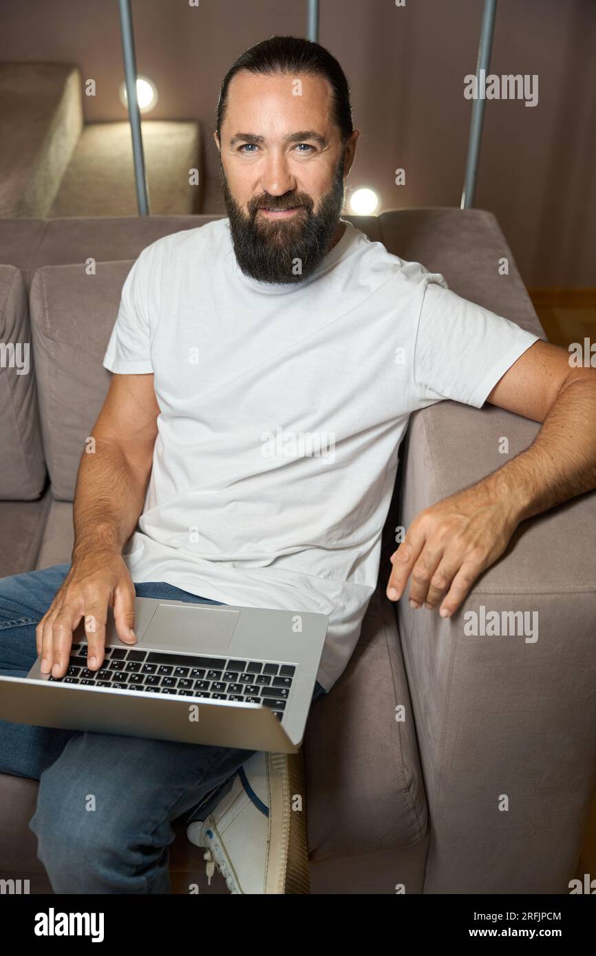 Handsome man sits on a sofa with a laptop Stock Photo