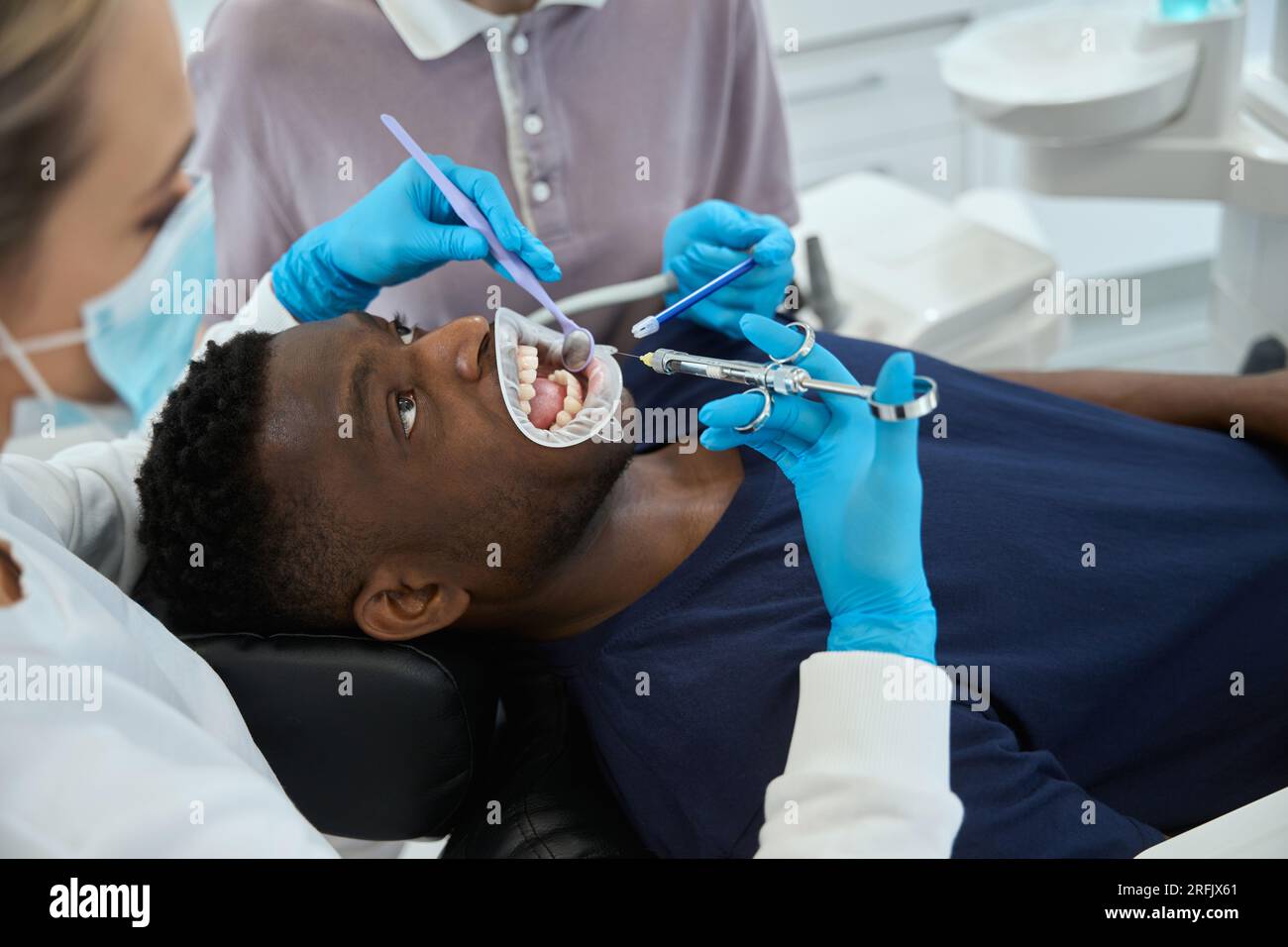 Nurse holding saliva ejector, assisting to female dentist who going to