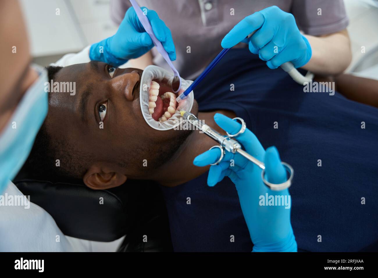 Woman dentist inserting mouth retractor to male client and doing anaesthetic injection before tooth treatment, root canal therapy or tooth extraction Stock Photo