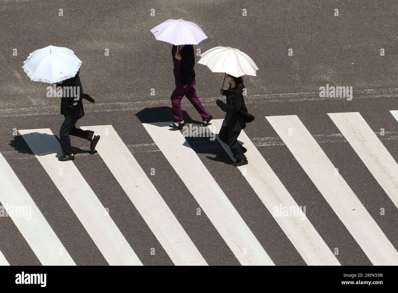 People, holding parasols, cross a street in scorching heat at Ginza