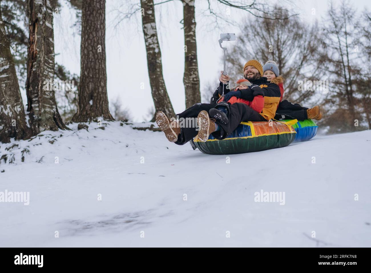 father and cute caucasian boys having a ride on snow tubing in winter ...
