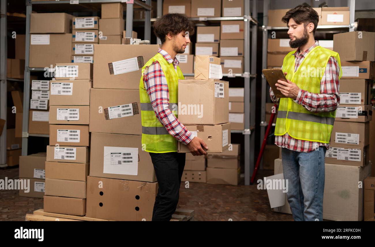 Warehouse manager using digital tablet doing inventory and courier with boxes preparing goods for shipment Stock Photo