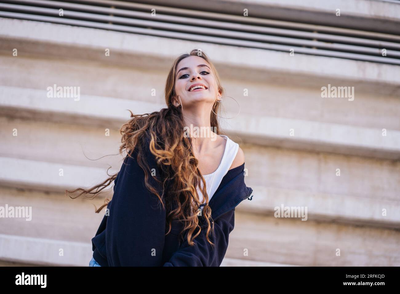 Cute Girl Smiling And Looking At Camera Next To A Concrete Wall. Stock Photo