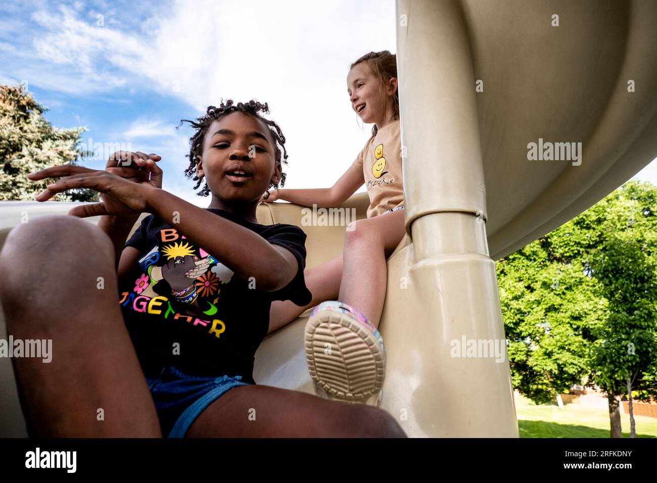 Friends going down slide at park together Stock Photo