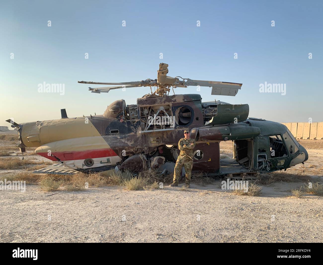 military man stands in front of crashed helicopter in desert Stock