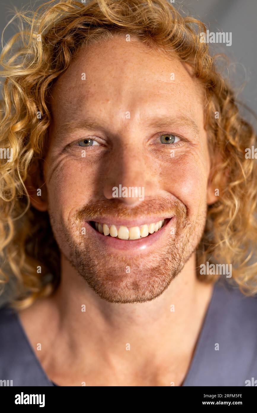 Portrait of happy caucasian male doctor with curly hair in corridor at hospital Stock Photo