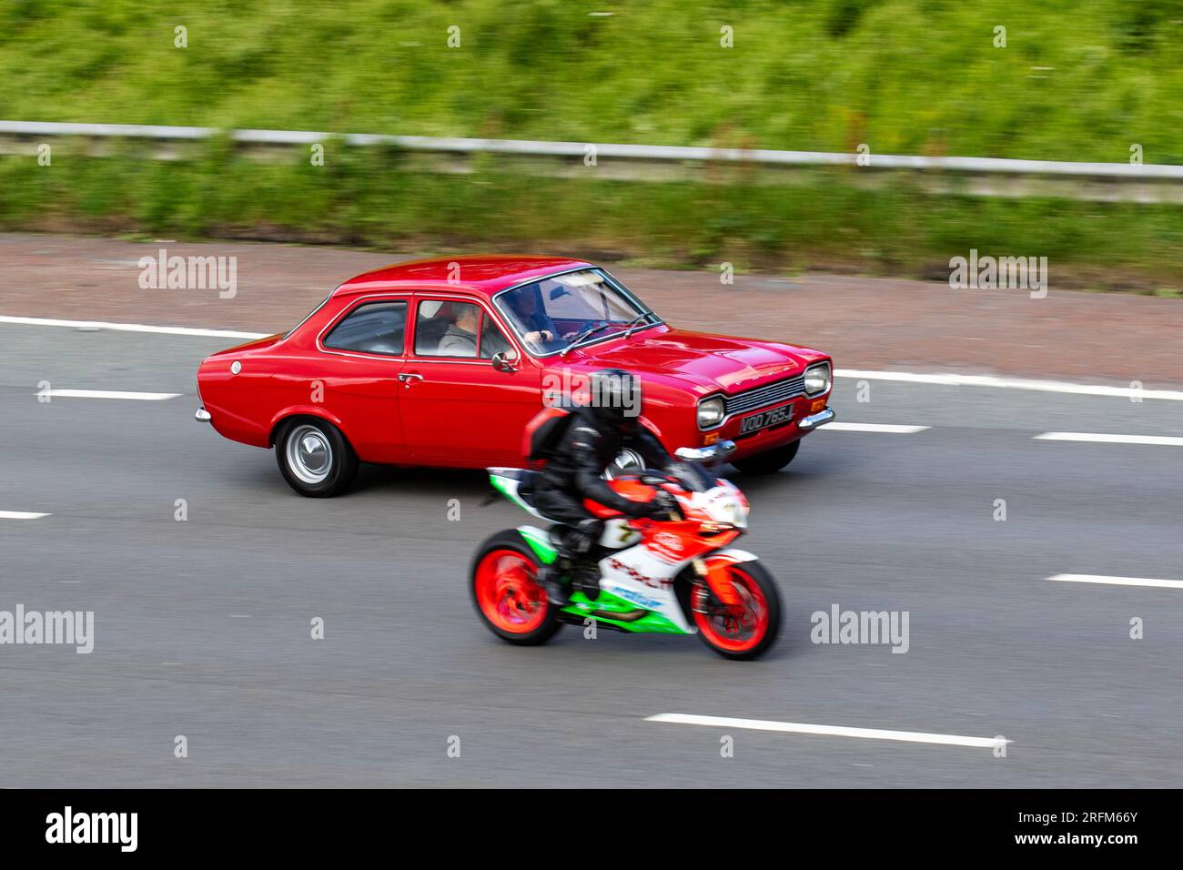 Honda CBR Motorcycle overtaking a 1970 70s seventies Red Ford Escort Lotus Petrol 1558 cc travelling at speed on the M6 motorway in Greater Manchester, UK Stock Photo