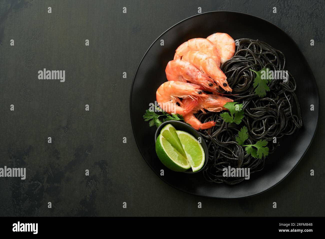 Black spaghetti pasta shrimp on black plate on dark concrete table background. Squid ink pasta with prawns. Pasta seafood. Top view on black stone tab Stock Photo