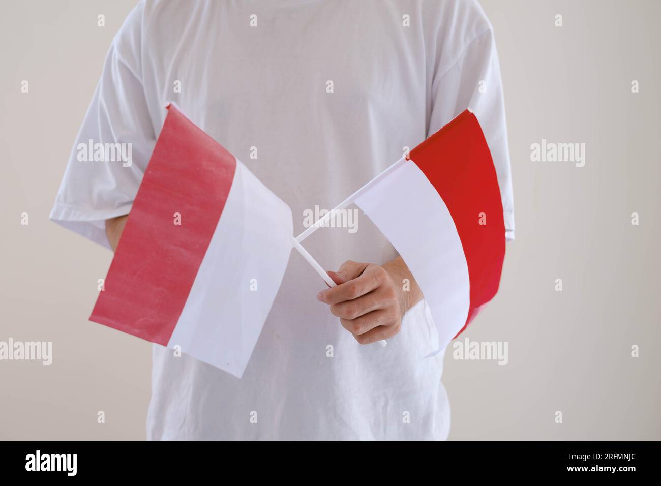 A man wearing white T-Shirt is holding Bendera Indonesia or Indonesian flag on isolated white background. Stock Photo