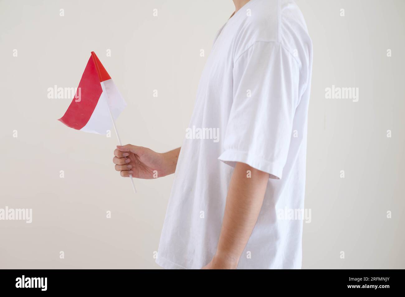 A man wearing white T-Shirt is holding Bendera Indonesia or Indonesian flag while facing the left side on isolated white background. Stock Photo