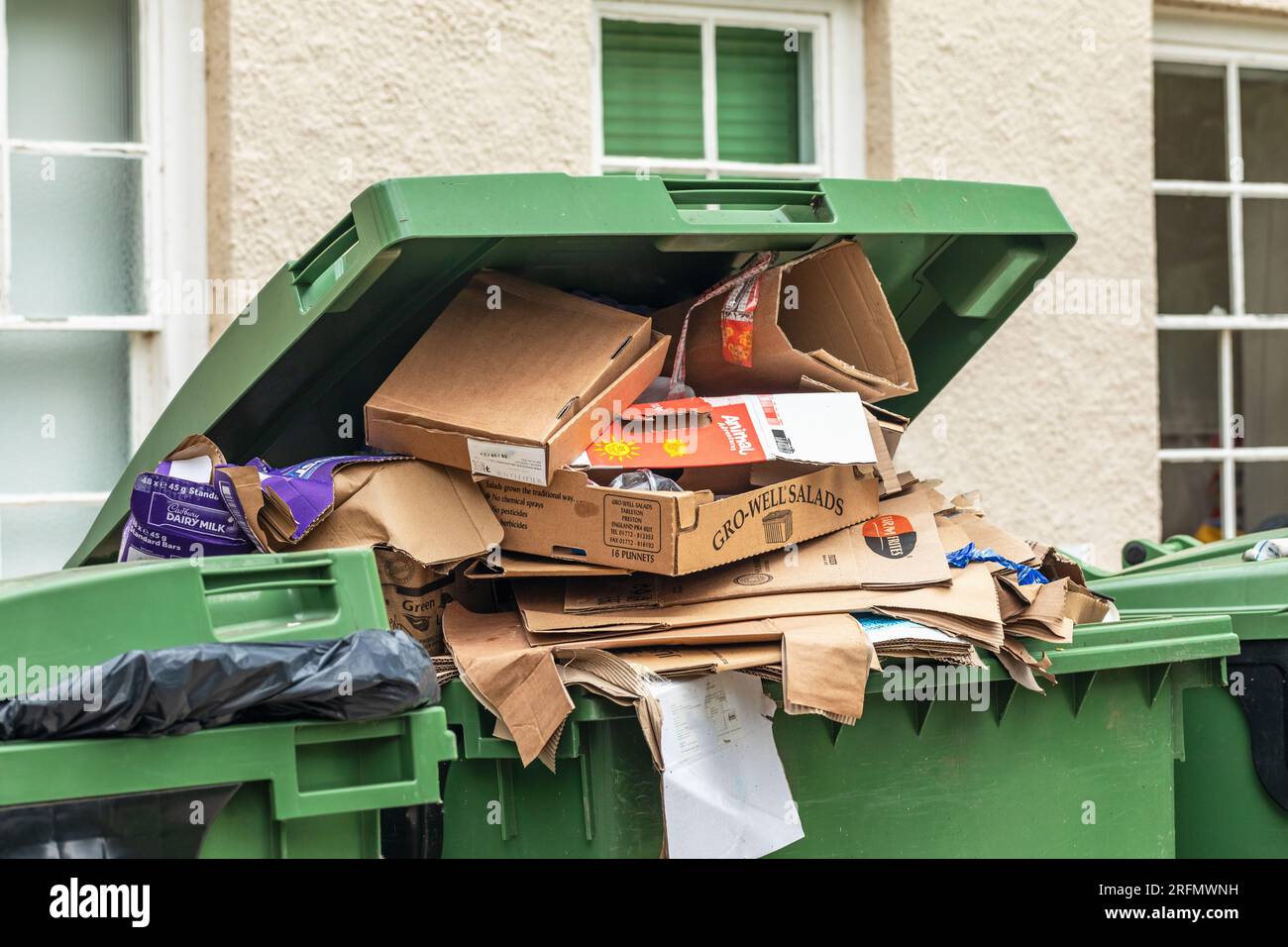 Overflowing filled cardboard recycling green bin awaiting collection