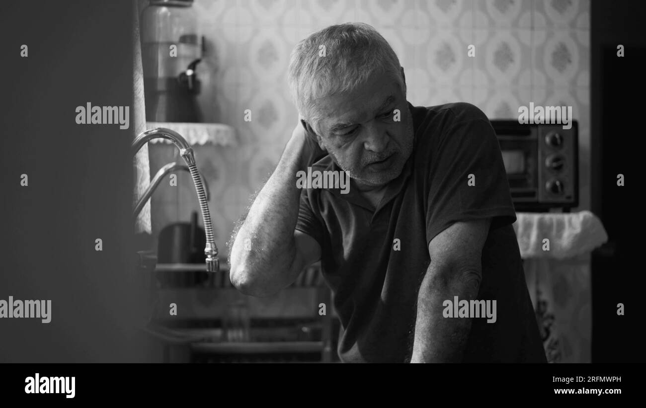 Senior man suffering from depression at home alone leaning by kitchen