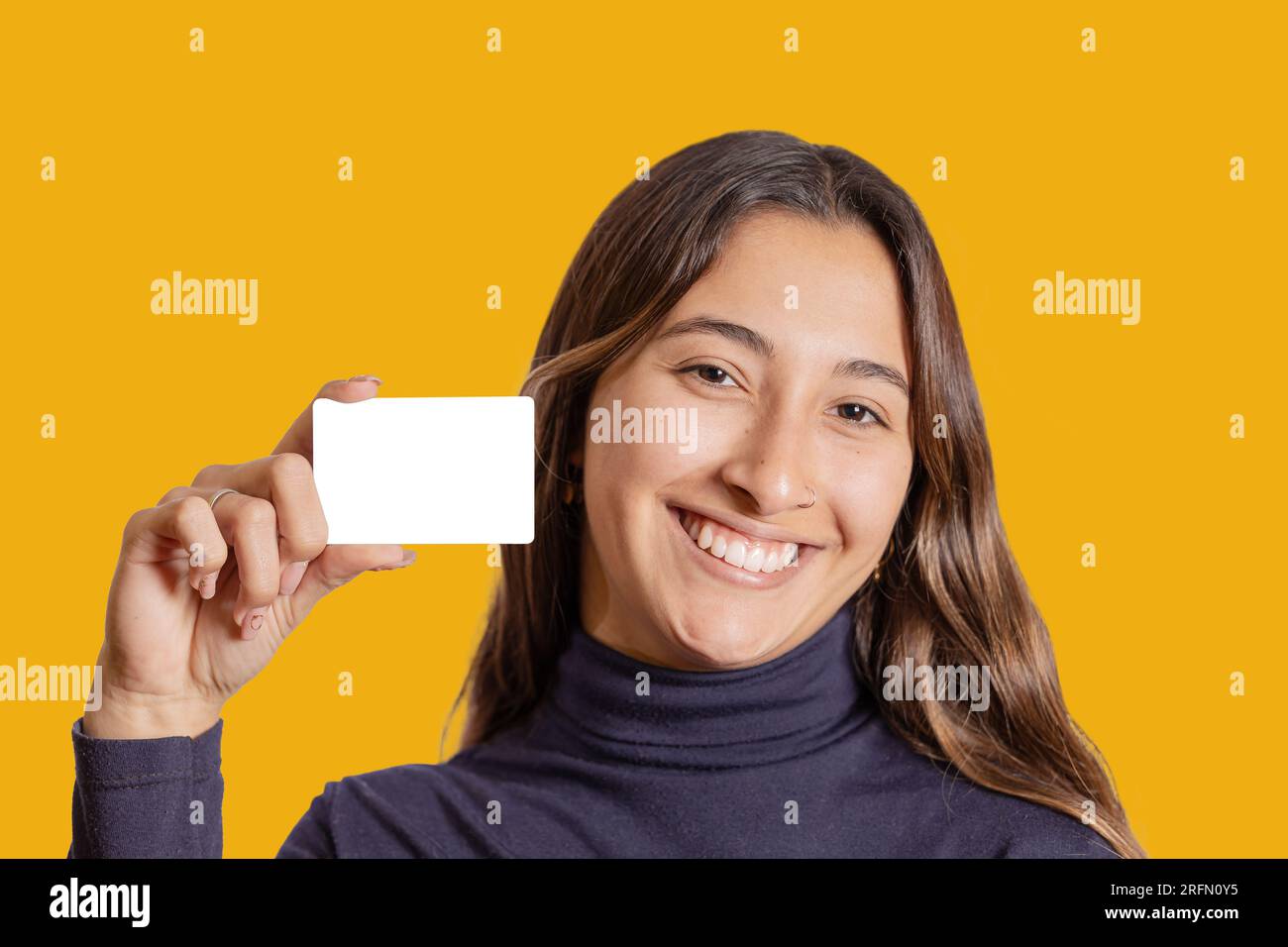 Portrait of smiling latina girl showing a blank card isolated on yellow background. Stock Photo