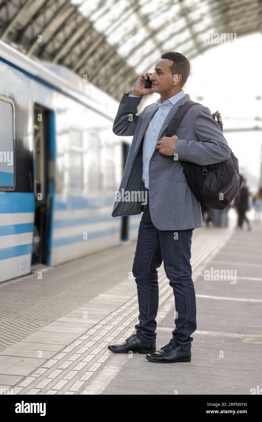 Latin man in a suit talking on the mobile phone at train station. Stock Photo