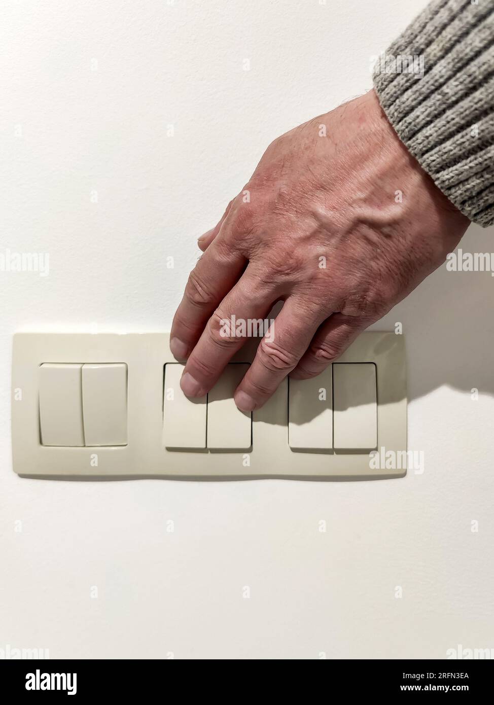 Man turns on the light. Man's hand in gray sweater presses light switch. Close-up. selective focus. Stock Photo