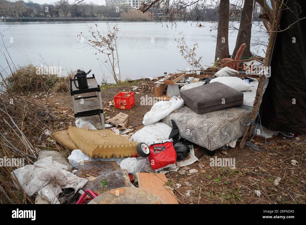 Austin Texas USA, January 2 2023: Trash and belongings from a long-time homeless camp line the north shore of Lady Bird Lake near Rainey Street in downtown Austin. City officials are struggling with homelessness issues along the popular hike and bike trails on public parkland that ring the lake. ©Bob Daemmrich Stock Photo