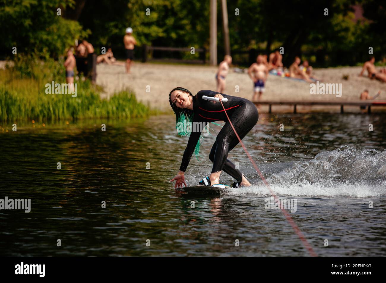 A girl in a wetsuit stands on a wakeboard on the river. Stock Photo