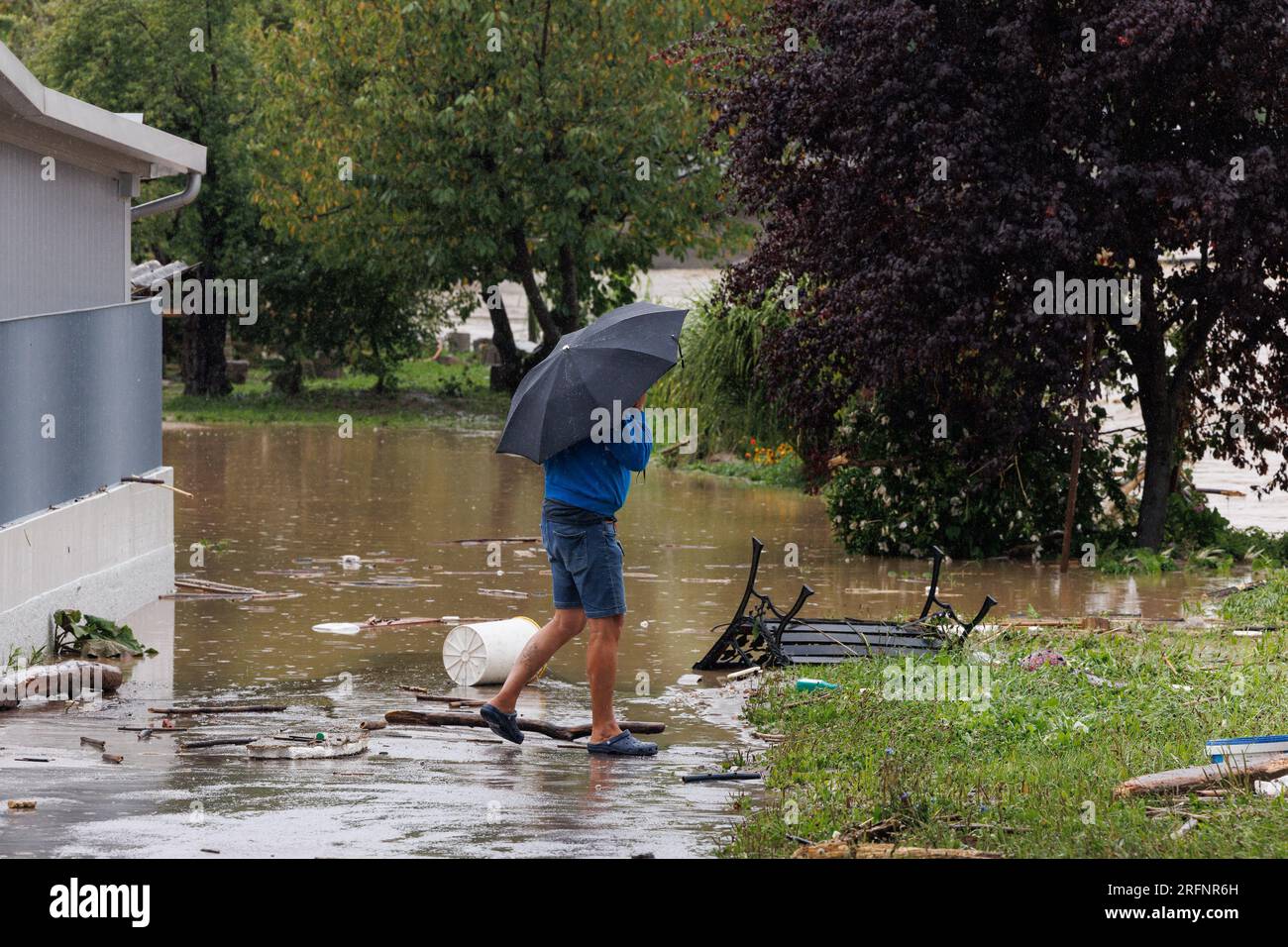 A man walks past a flooded driveway after a flood in Medvode. Heavy continuous torrential rain and storms have caused major flooding all throughout Slovenia in the first part of the forecasted severe weather event. Roads and railroads were closed, several areas had no electricity or drinking water, and fatalities were reported. Stock Photo
