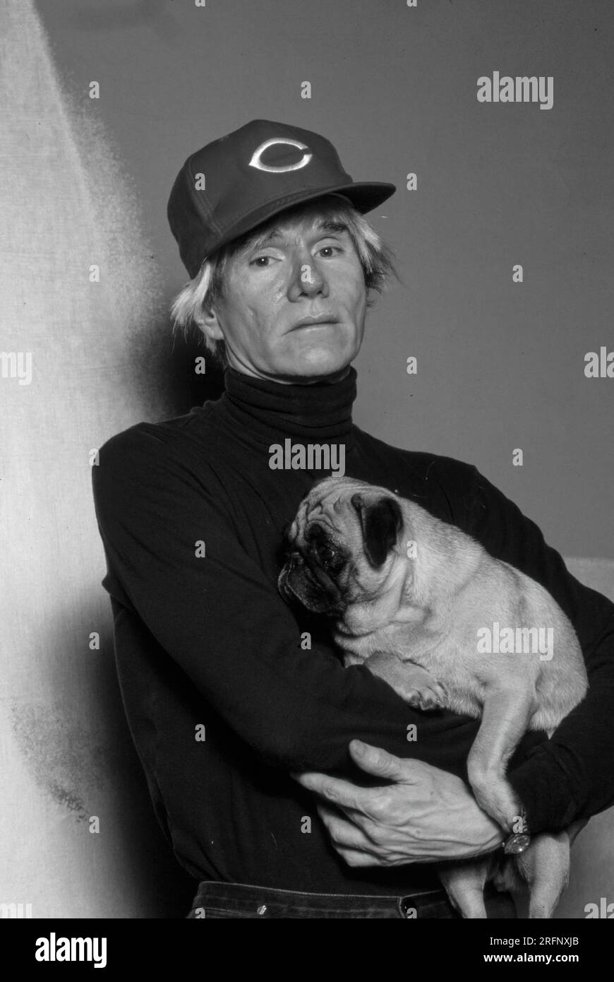 Andy Warhol poses wearing Cincinnati Reds baseball cap while holding